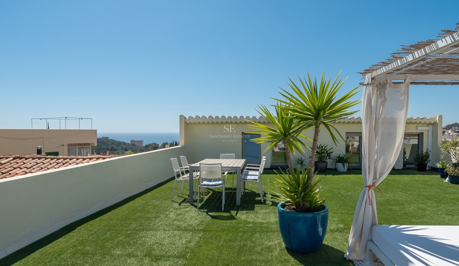Dachterrasse mit Kunstrasen, Essbereich und einem Tagesbett mit Vorhängen und Blick auf das Mittelmeer.