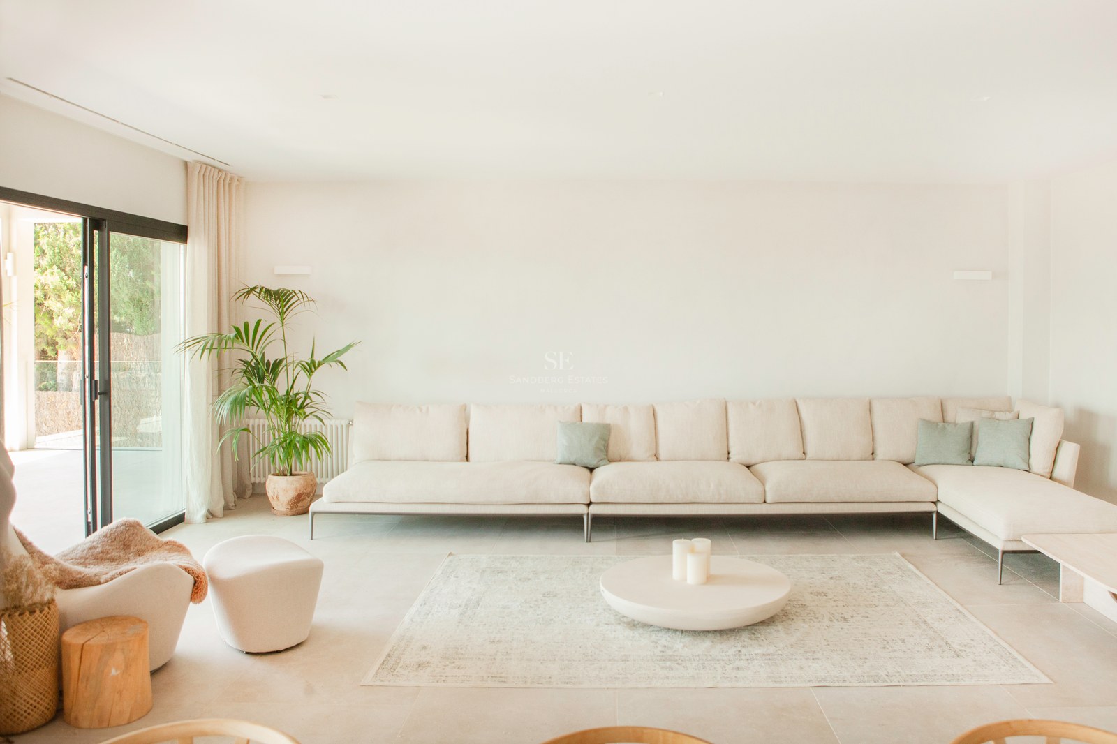 Helles Wohnzimmer mit großem beigem Ecksofa, rundem Couchtisch auf Teppich und Glasschiebetüren zur Terrasse.