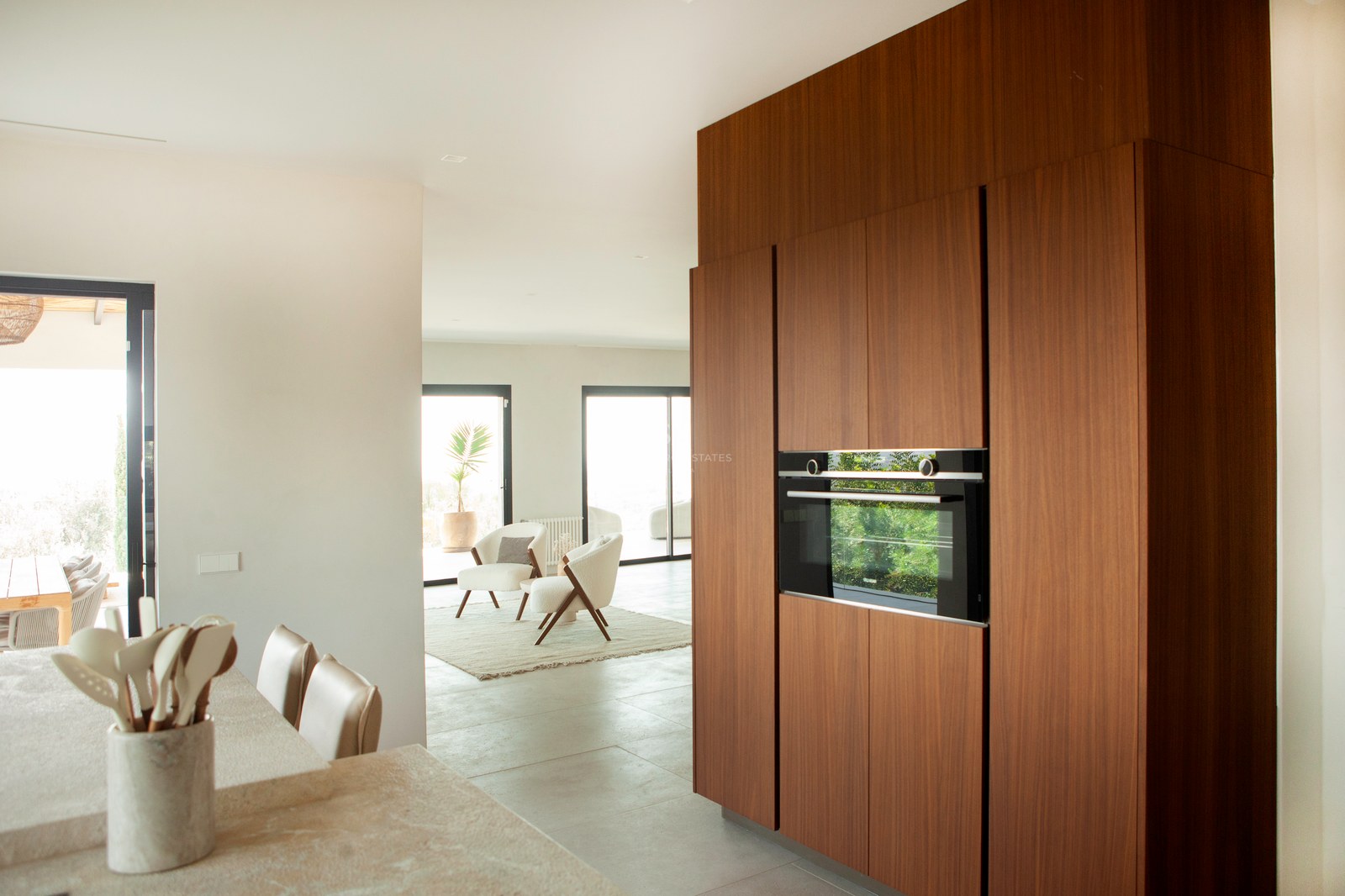 Moderne Küche mit Walnussholzschränken, Einbaubackofen und Steininsel mit Blick auf das helle Wohnzimmer.