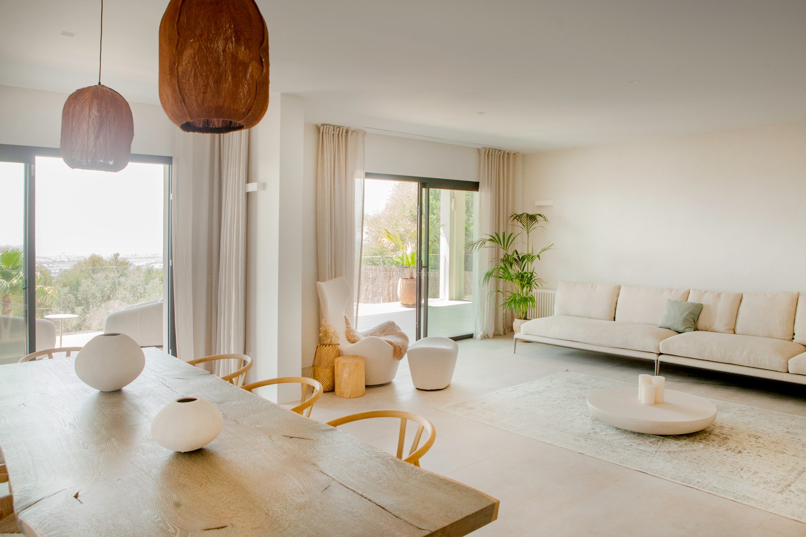 Helles modernes Wohnzimmer mit großem Holzesstisch, weißem Sofa und bodentiefen Fenstern zur Terrasse.
