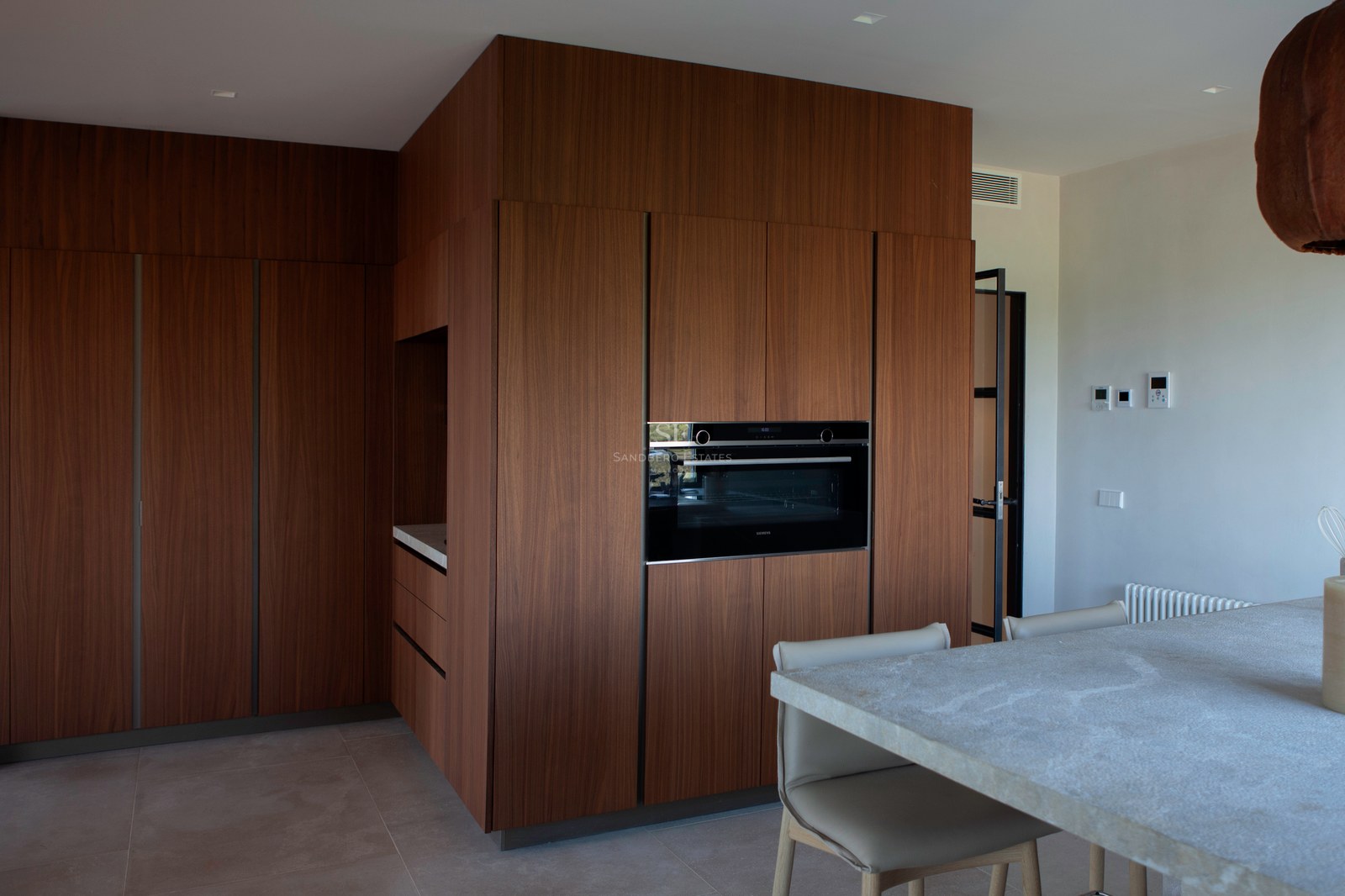 Moderne Küche mit raumhohen Walnussholz-Schränken, integriertem Backofen und Steininsel mit Lederstühlen.