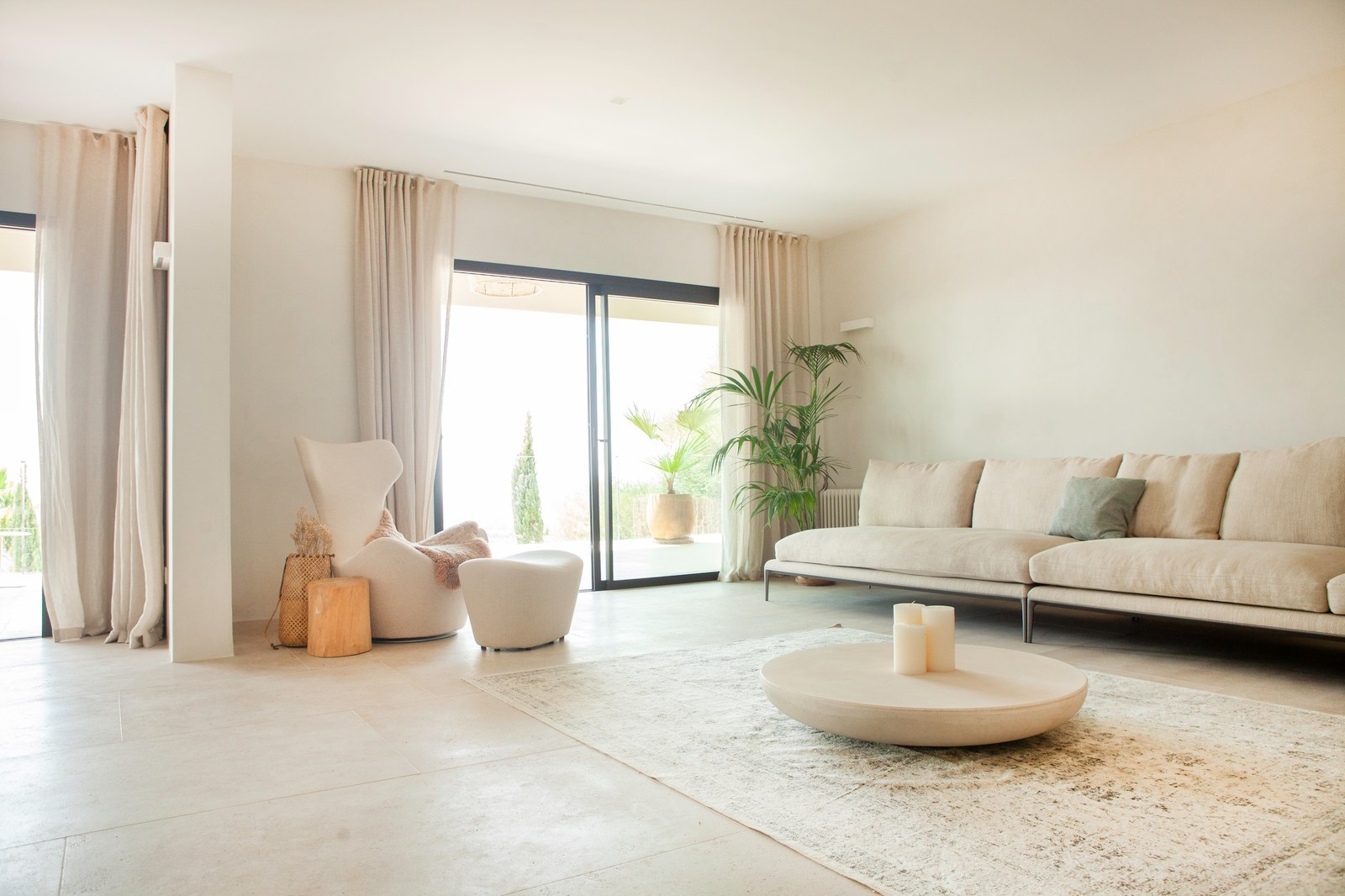 Helles Wohnzimmer mit beige Sofa, Steincouchtisch und bodentiefe Fensterfronten zur Terrasse.