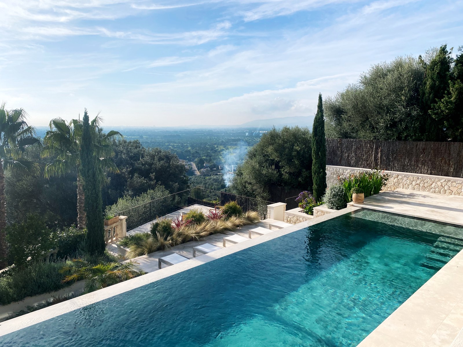 Türkisfarbener Infinity-Pool mit Blick auf eine üppige grüne Landschaft unter klarem blauem Himmel.