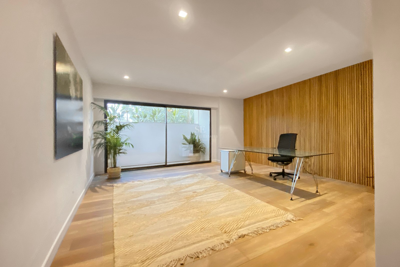 Modernes Arbeitszimmer mit Glastisch, Holzlamellenwand und Glasschiebetür zu einem kleinen Innenhof.