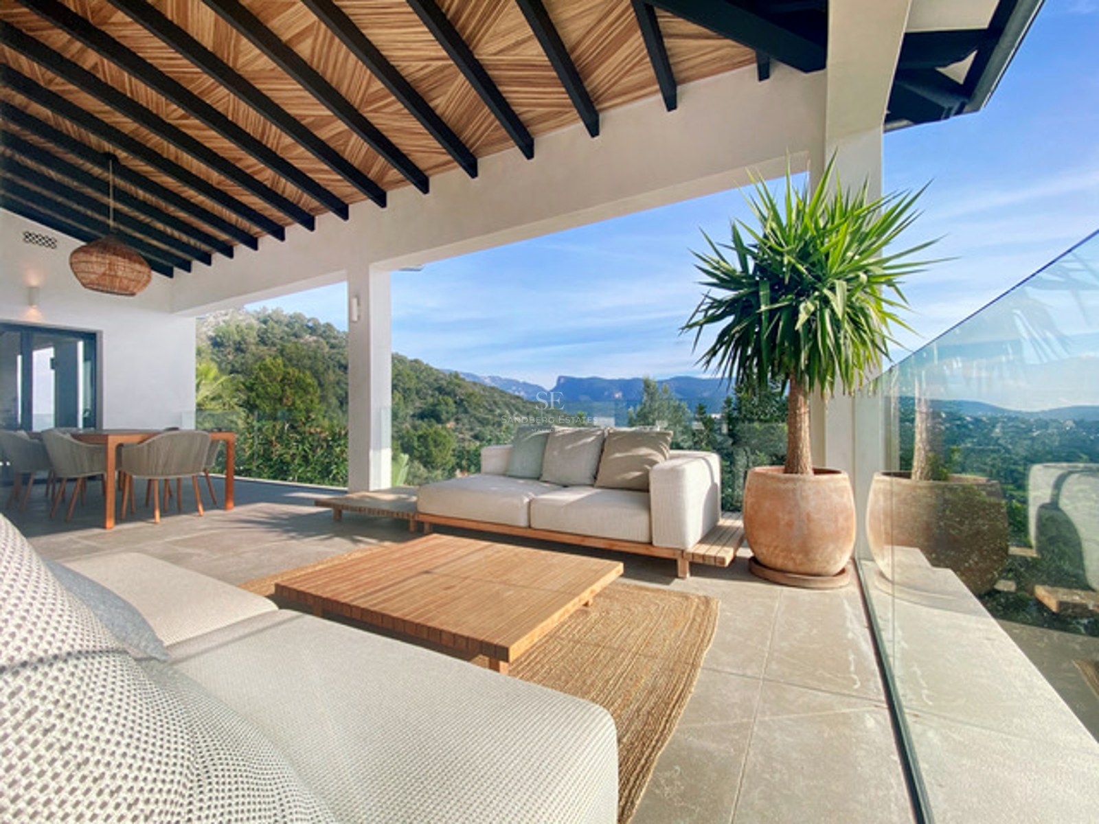 Moderne überdachte Terrasse mit Loungemöbeln, Holzbalkendecke und weitem Blick auf grüne Berge.