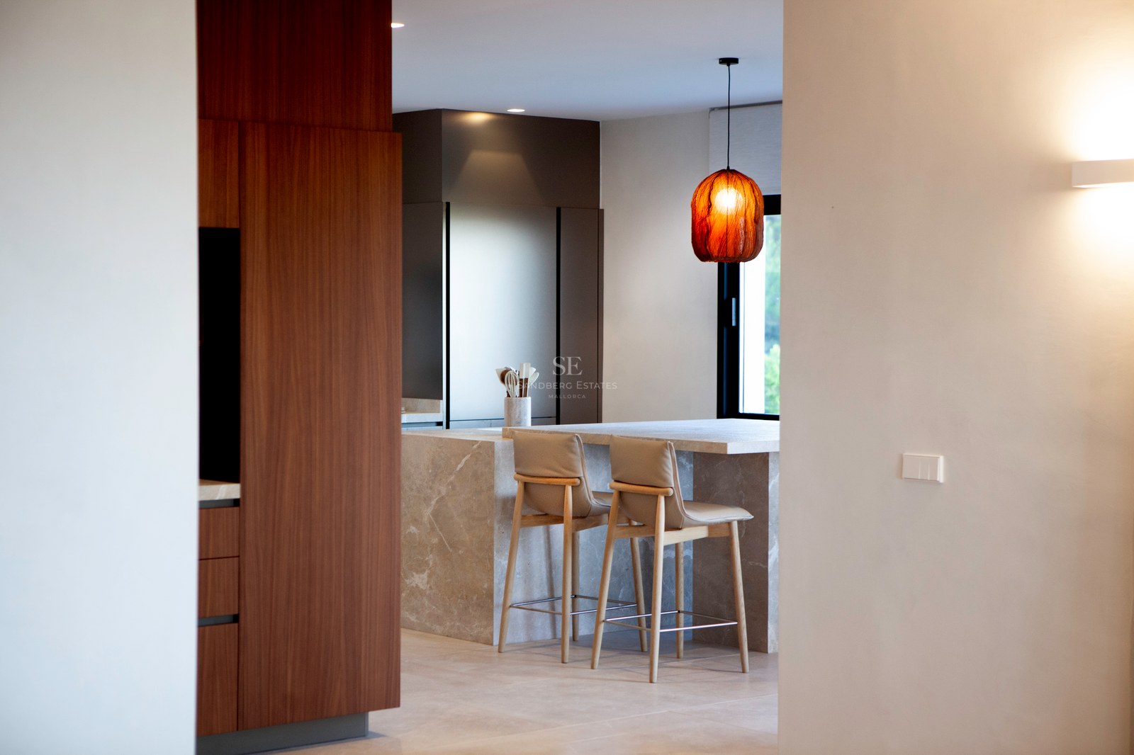 Moderne Küche mit großer Steininsel, Barhockern, Schränken aus Walnussholz und Designer-Leuchte.