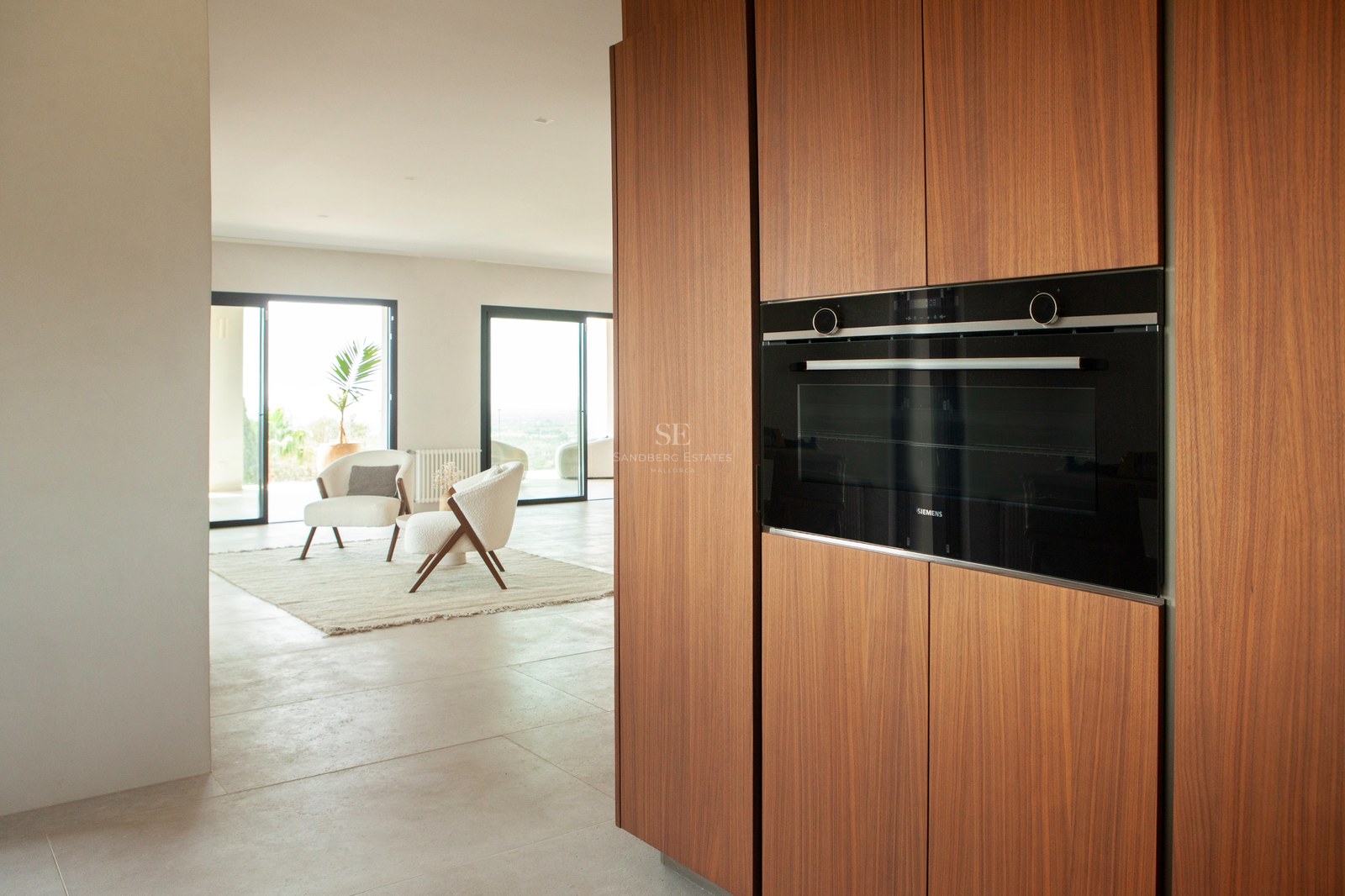 Nahaufnahme von Walnussholz-Küchenschränken mit eingebautem Siemens-Backofen mit Blick auf ein helles Wohnzimmer.