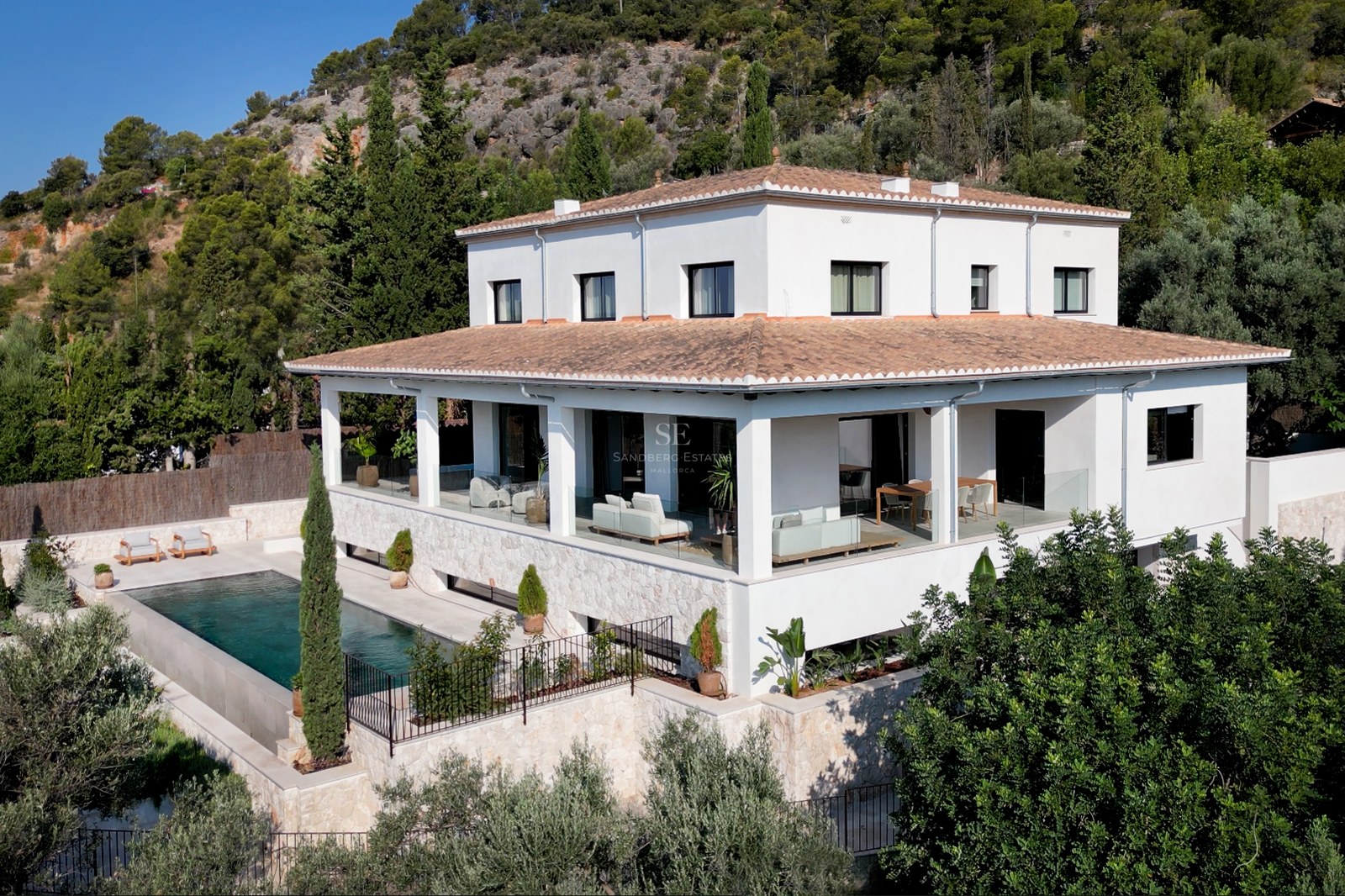 Erhöhte Ansicht einer weißen mehrstöckigen Villa mit Ziegeldach, Pool und Natursteinterrassen im Grünen.