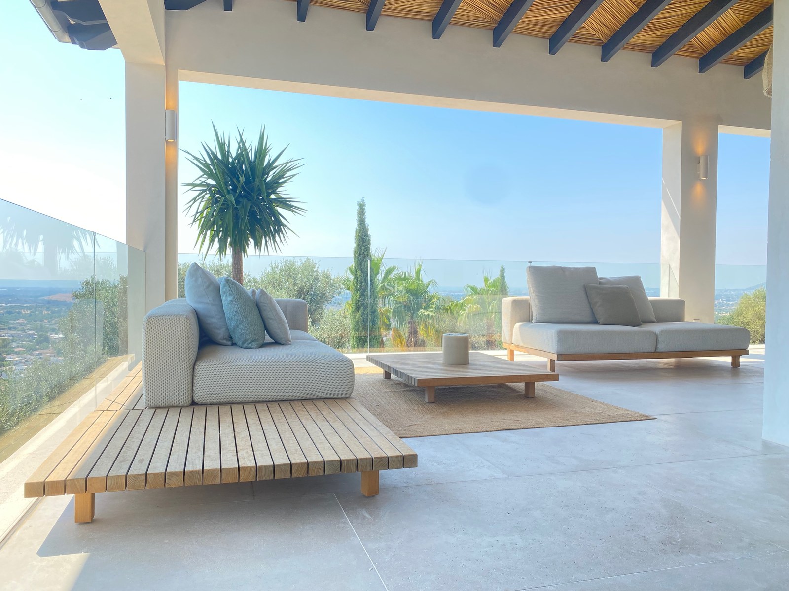 Luxuriöse Terrasse mit modernen Sofas, Holztisch, Glasgeländer und weitem Blick auf die Landschaft.