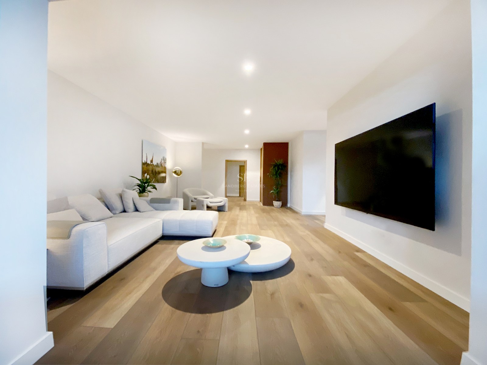 Modernes Wohnzimmer mit weißem Ecksofa, runden Couchtischen, hellem Holzboden und großem Flachbildfernseher.