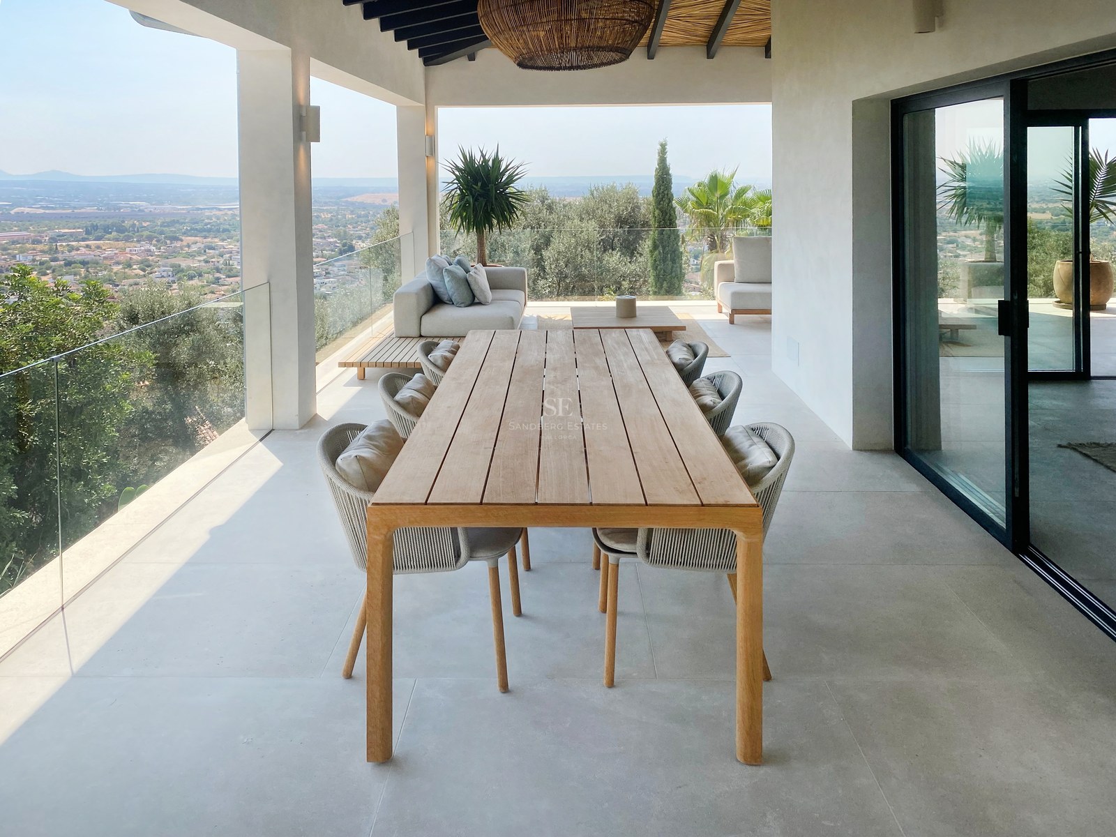 Weitläufige überdachte Terrasse mit Holzesstisch, modernem Loungebereich und Glasgeländer mit Blick auf das Tal.