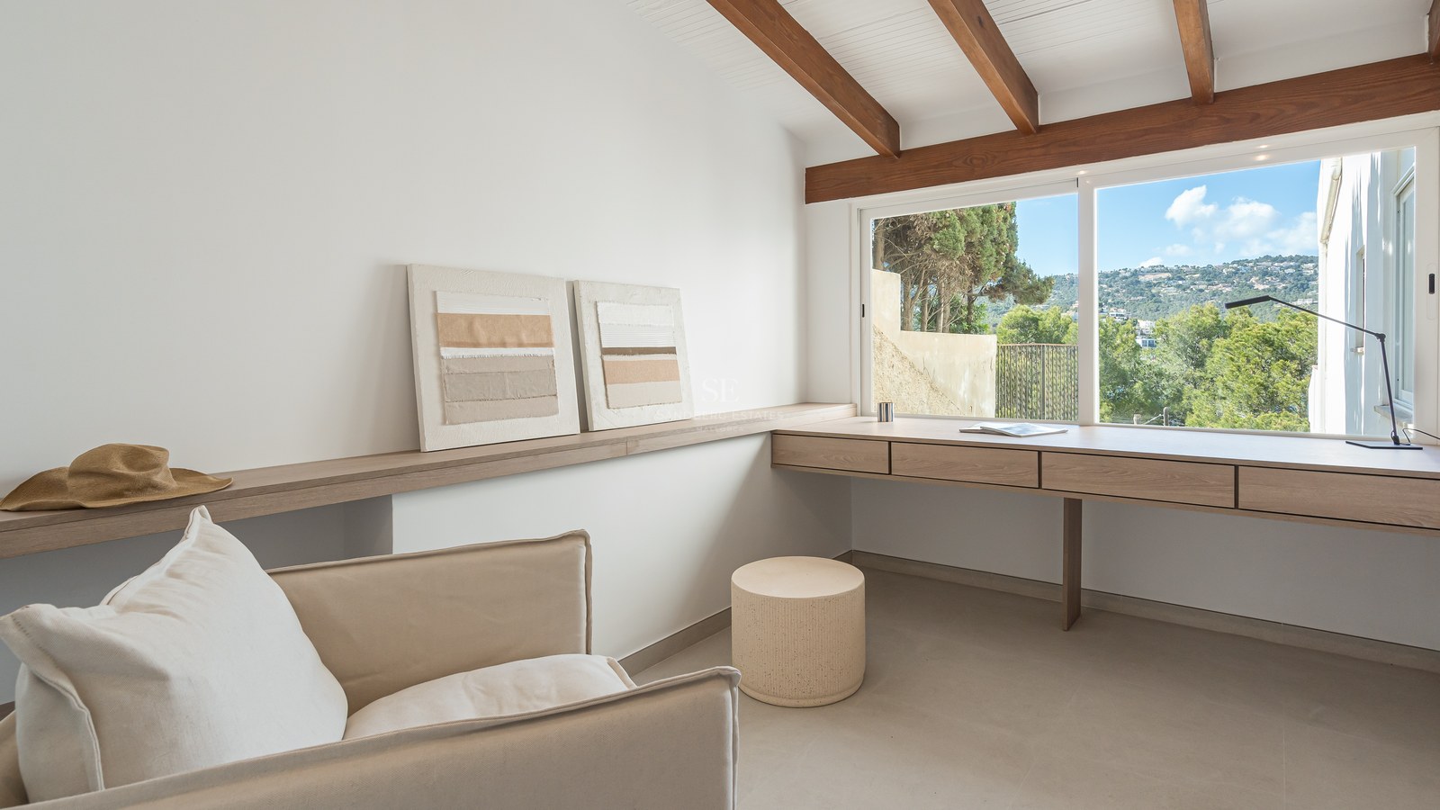 Oficina luminosa con escritorio de roble integrado, vigas de madera a la vista y ventana con vistas a la vegetación.