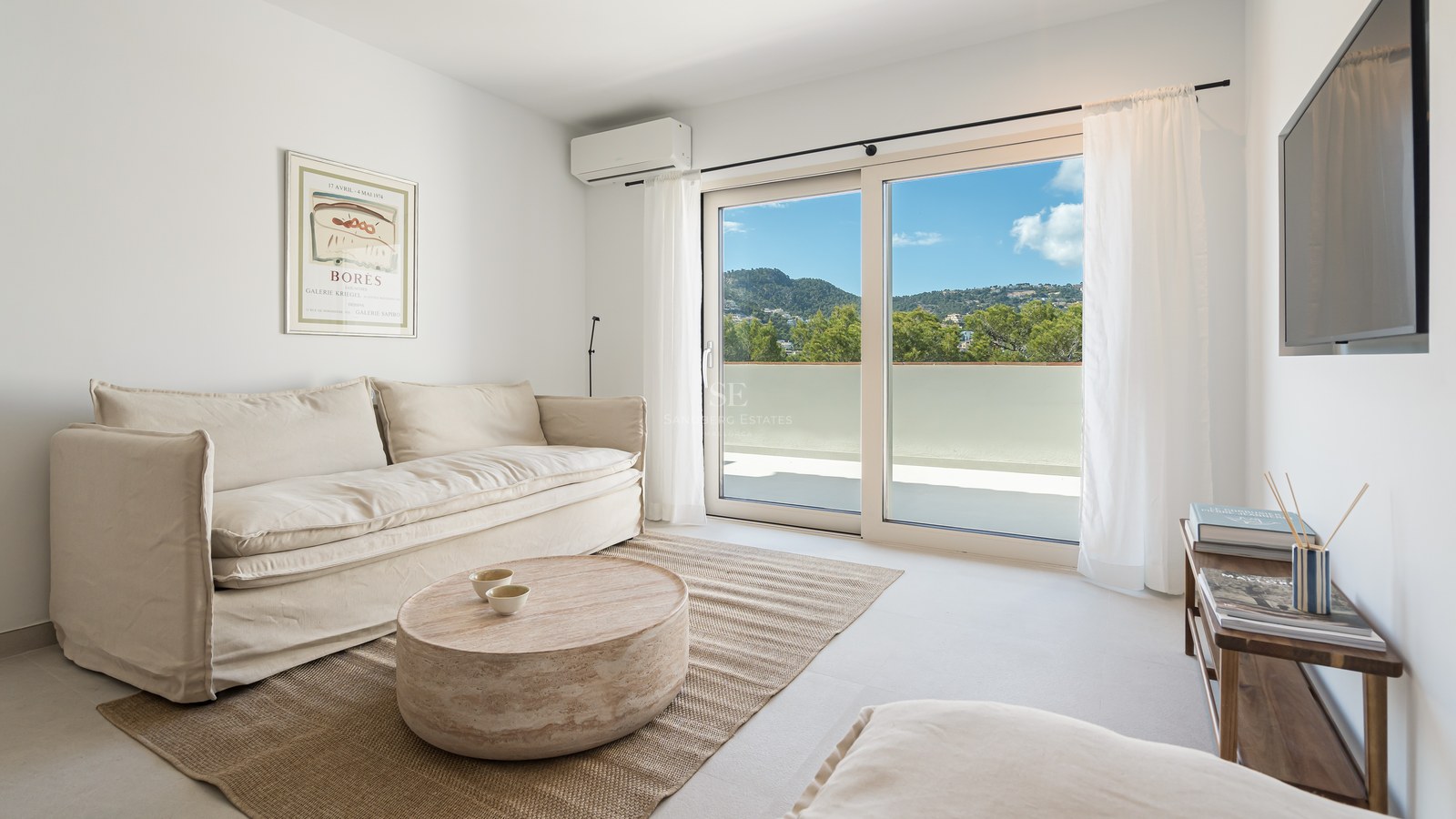 Salón moderno con sofá de lino blanco y grandes ventanales con vistas a la vegetación de montaña.