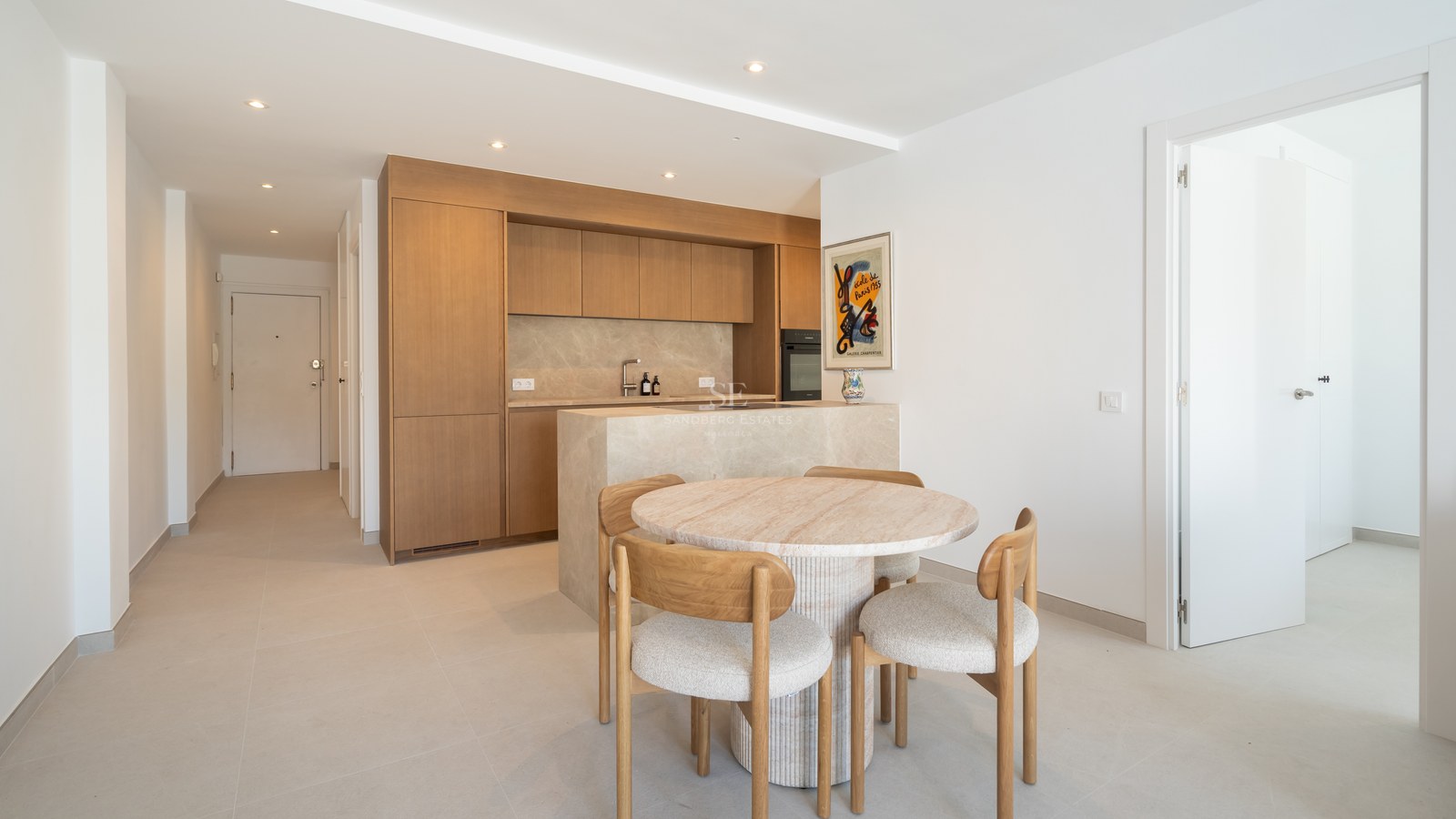 Cocina contemporánea con armarios de roble claro, isla de mármol y mesa circular de piedra con sillas de madera.