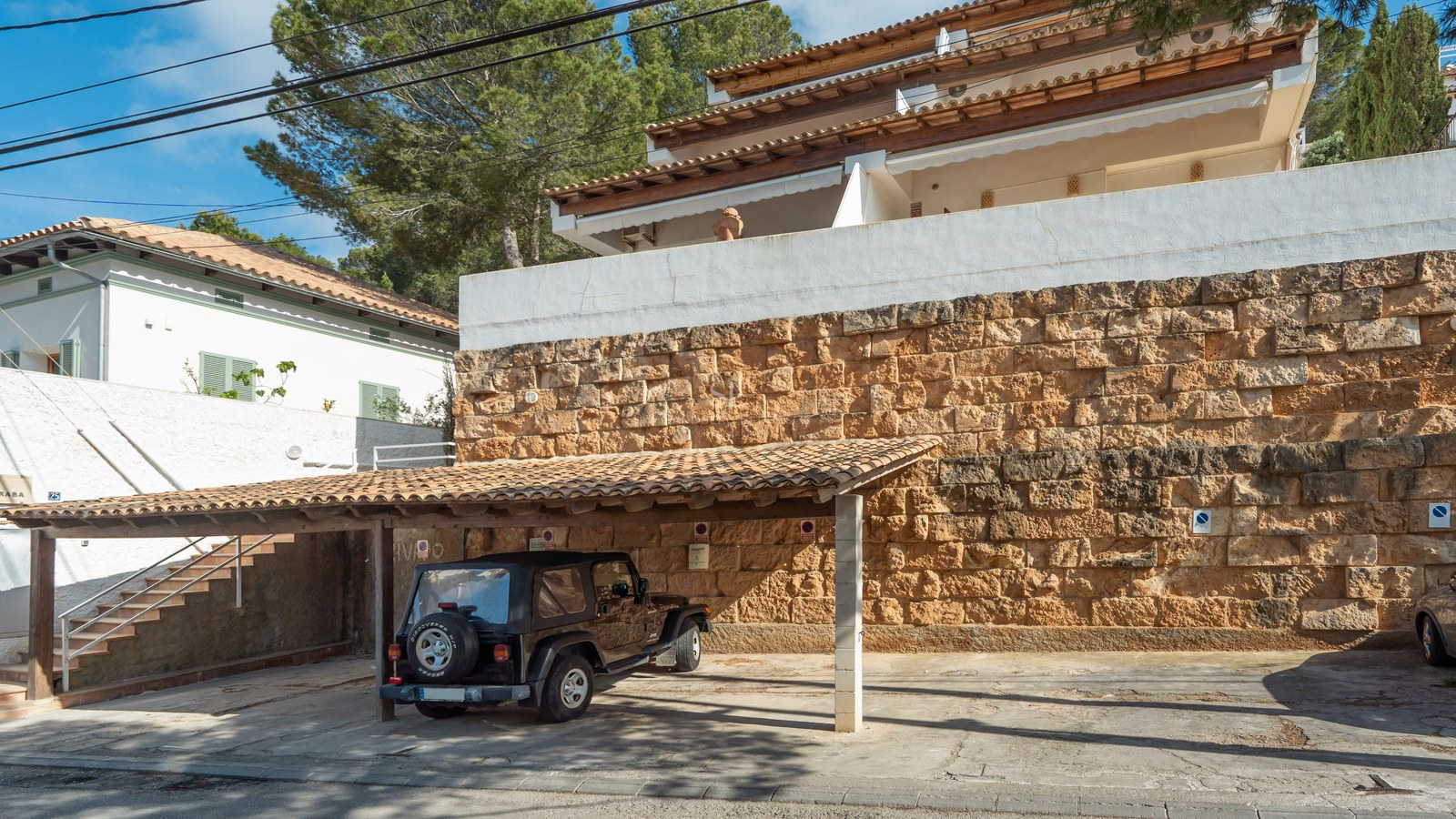 Vehículo todoterreno negro bajo un aparcamiento cubierto con techo de tejas y una robusta pared de piedra natural.