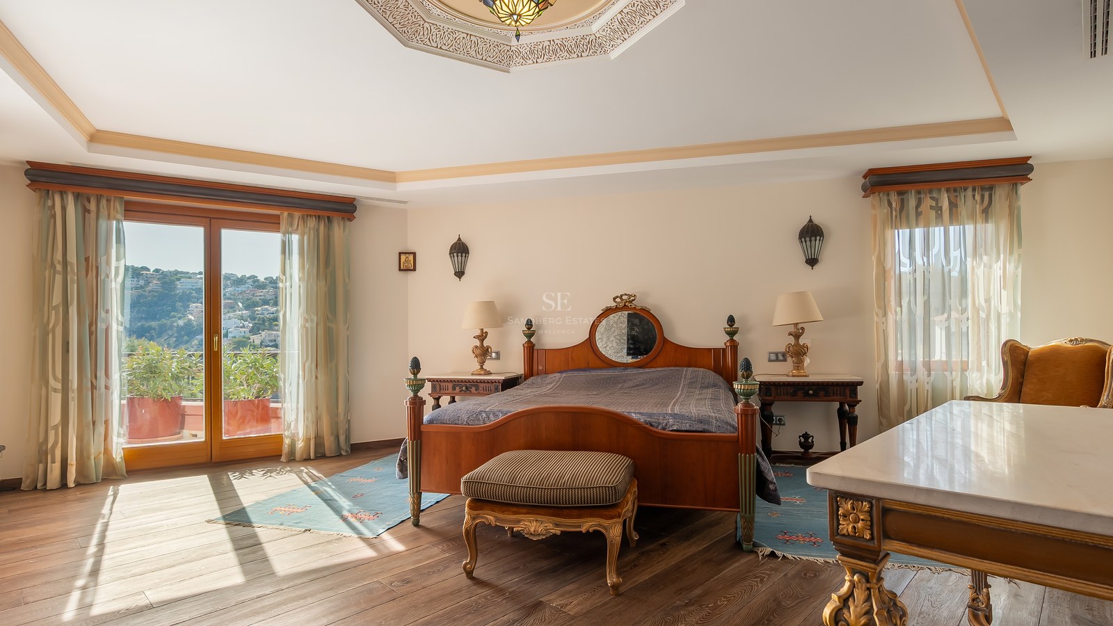 Chambre de style traditionnel avec un lit en bois, plafond orné et porte vitrée menant à un balcon.