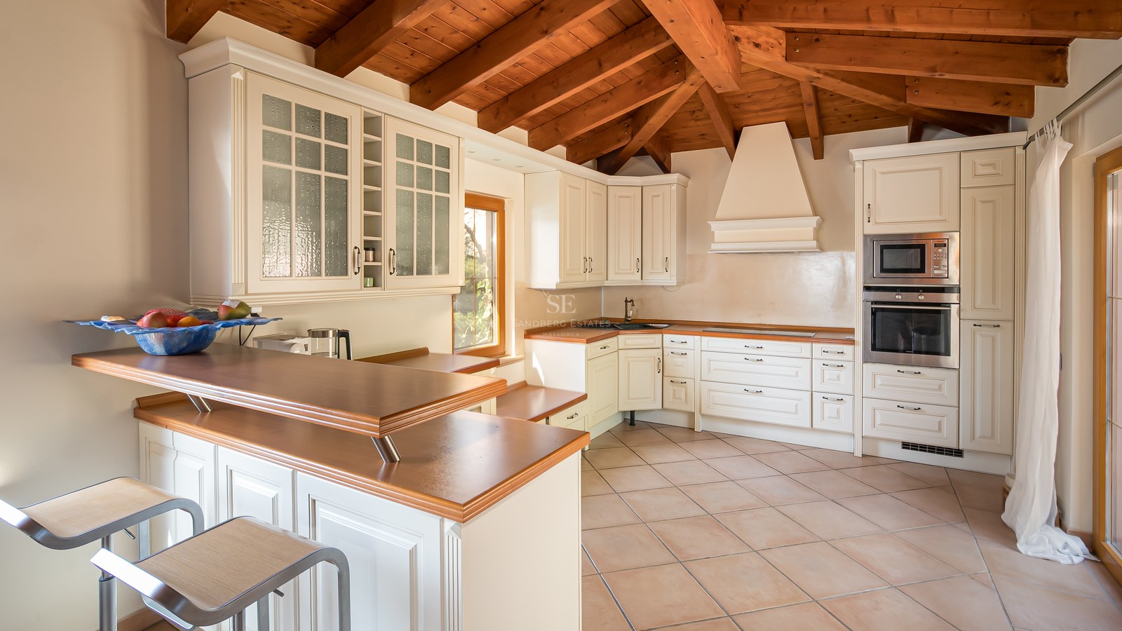 Cuisine rustique avec placards blancs, plans de travail en bois et poutres en bois massif au plafond.