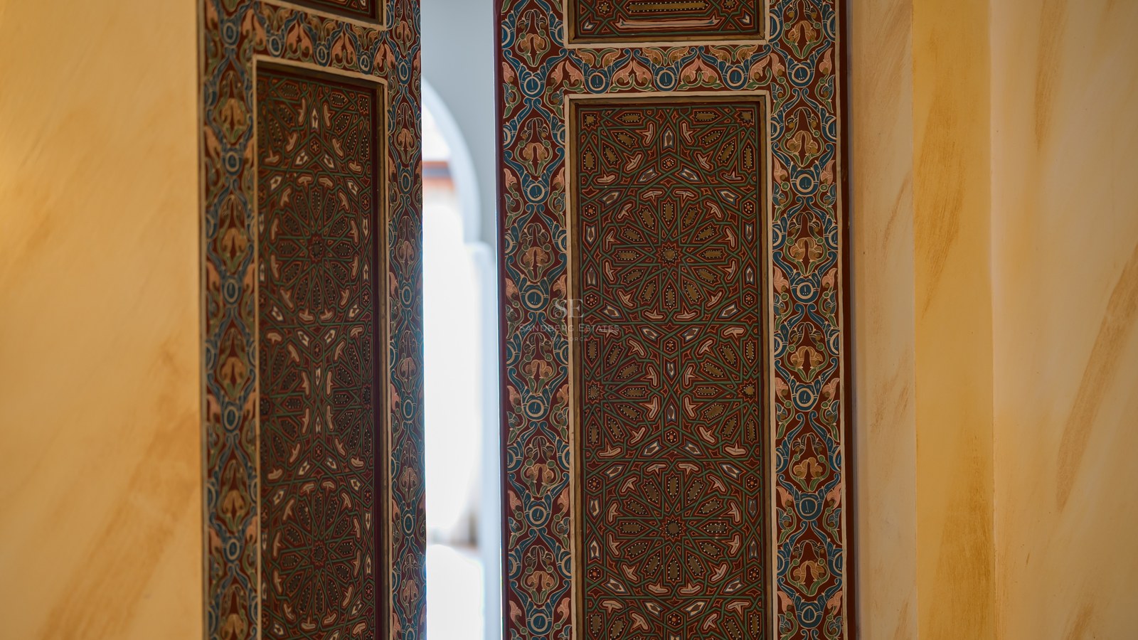 Motifs mauresques complexes sur une porte en bois sombre s'ouvrant sur un patio lumineux.