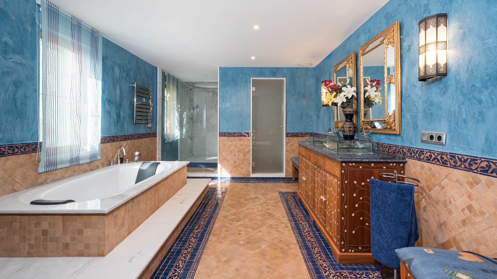 Salle de bain de prestige avec baignoire intégrée, meuble en bois travaillé, miroirs dorés et murs bleus texturés.