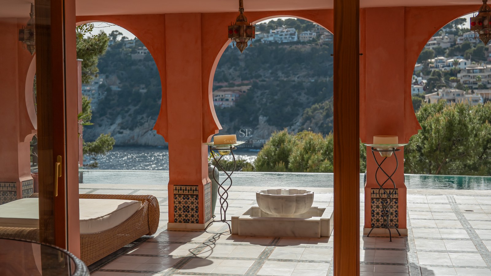 Terrasse couverte avec arches terracotta et colonnes carrelées surplombant une baie bleue et des collines vertes.