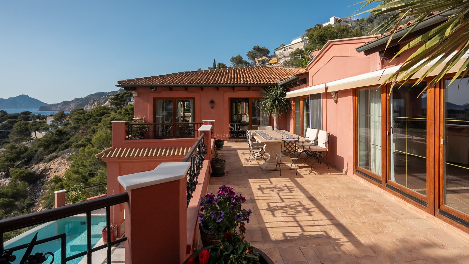 Terrasse ensoleillée avec table en pierre, tuiles en terre cuite et balustrades en fer forgé dominant le paysage.
