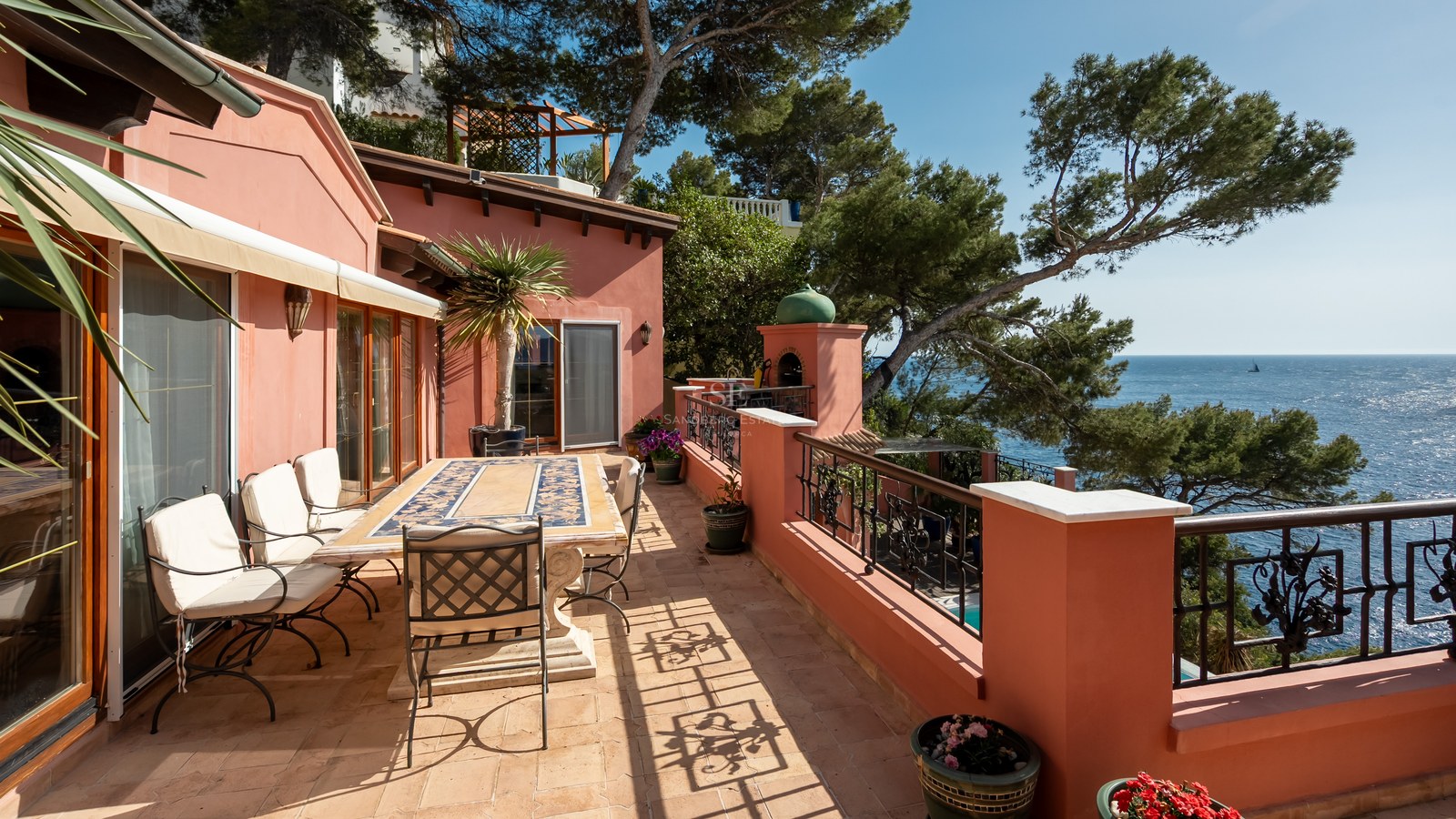 Terrasse en terre cuite avec table à manger, ferronnerie d'art et vue mer à travers les pins.