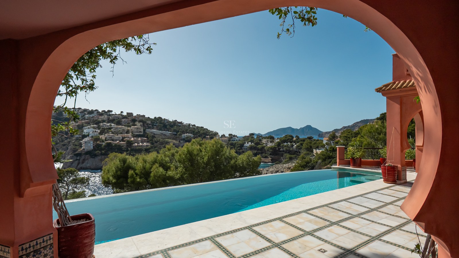 Une piscine à débordement aux eaux turquoise surplombant des collines verdoyantes et des villas de luxe.