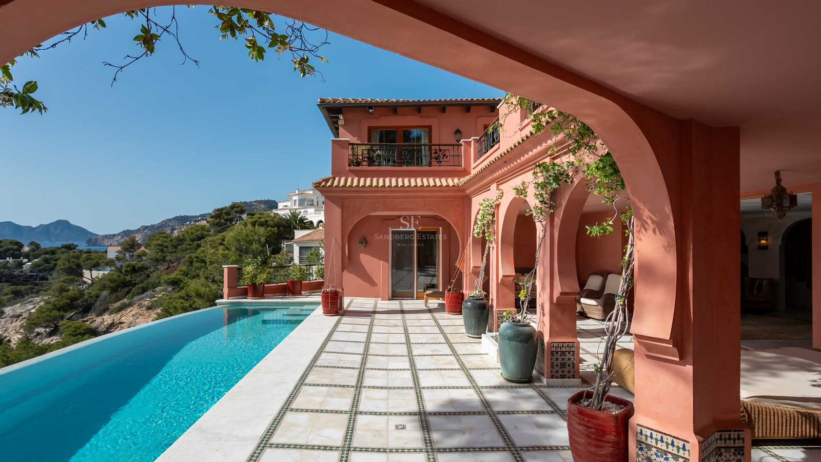 Villa de luxe aux tons terracotta avec piscine à débordement, terrasse voûtée et vue sur la côte.