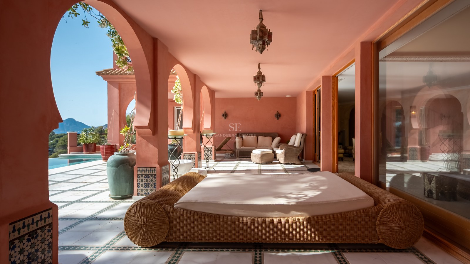 Terrasse ombragée aux murs terracotta avec arches, lits de repos en osier et lanternes artisanales.