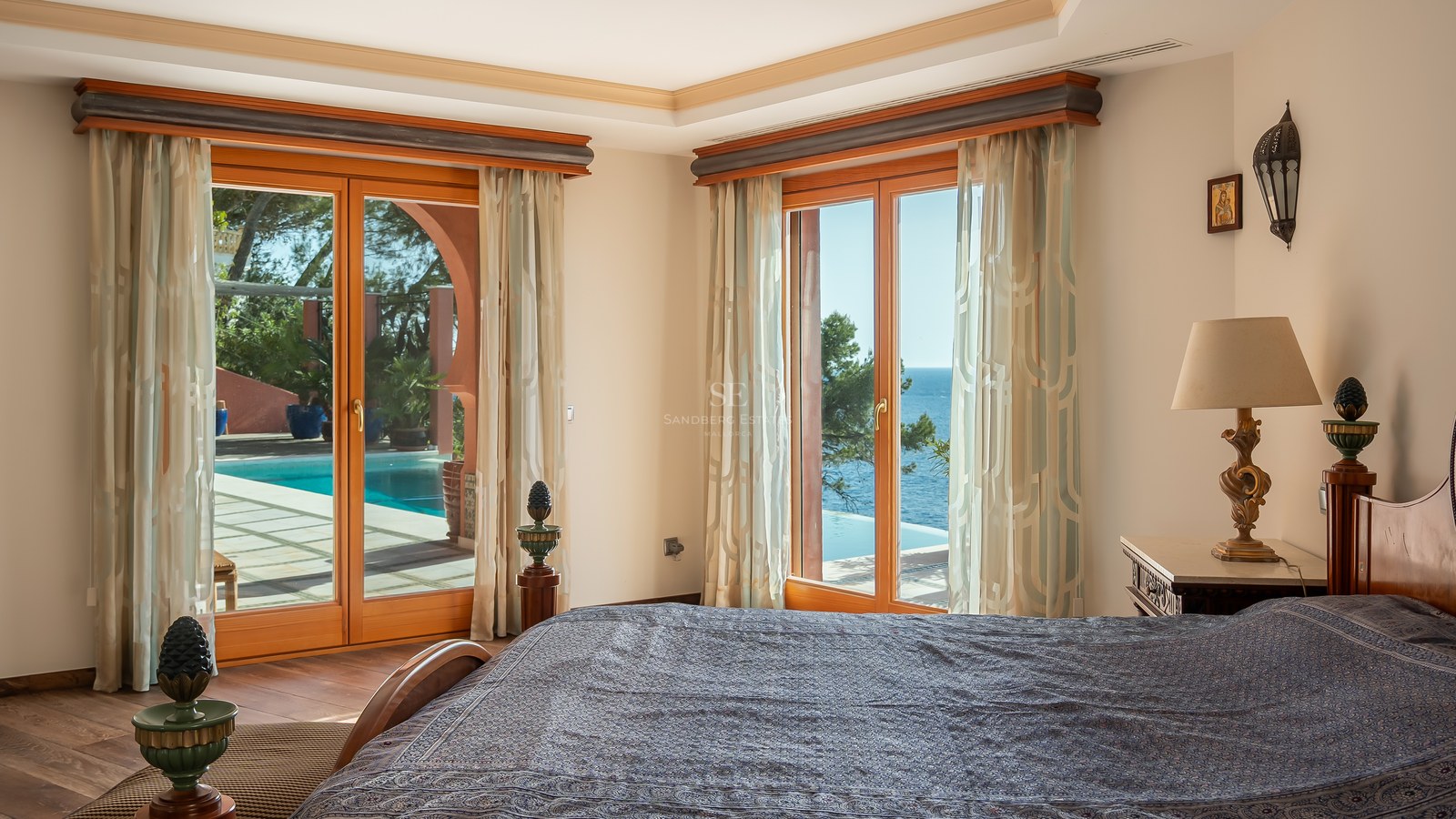 Chambre principale avec de grandes fenêtres en bois s'ouvrant sur une terrasse avec piscine et vue sur la mer.