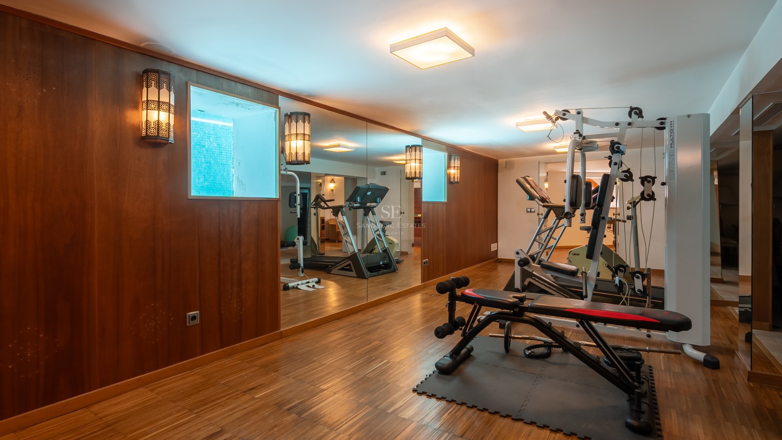 Salle de sport à domicile avec parquet, murs miroir, tapis de course et banc de musculation.