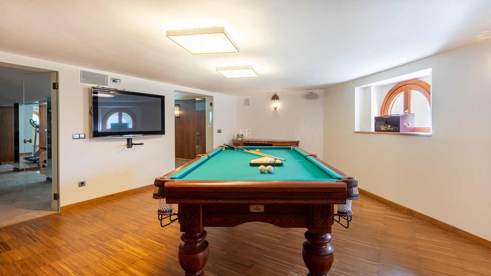 Table de billard en bois et tapis vert dans une salle de jeux moderne avec parquet et télévision murale.