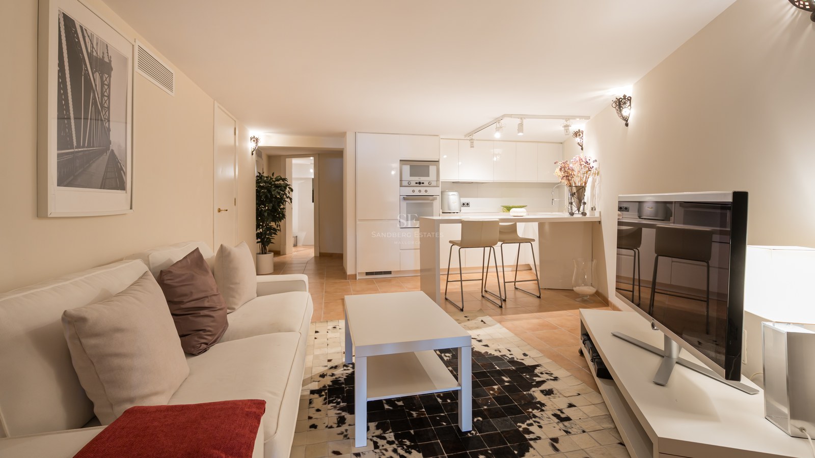 Salon moderne à aire ouverte avec canapé blanc, tapis en peau de vache et cuisine intégrée blanche avec comptoir.