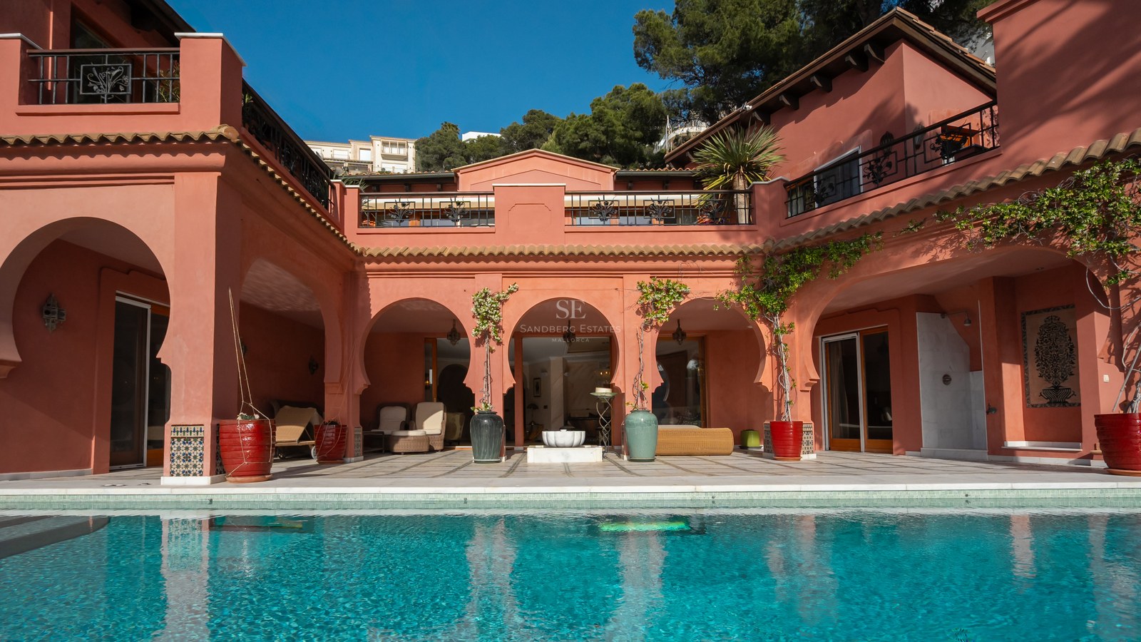 Façade de villa de luxe aux murs terre cuite avec arches mauresques donnant sur une piscine bleu turquoise.