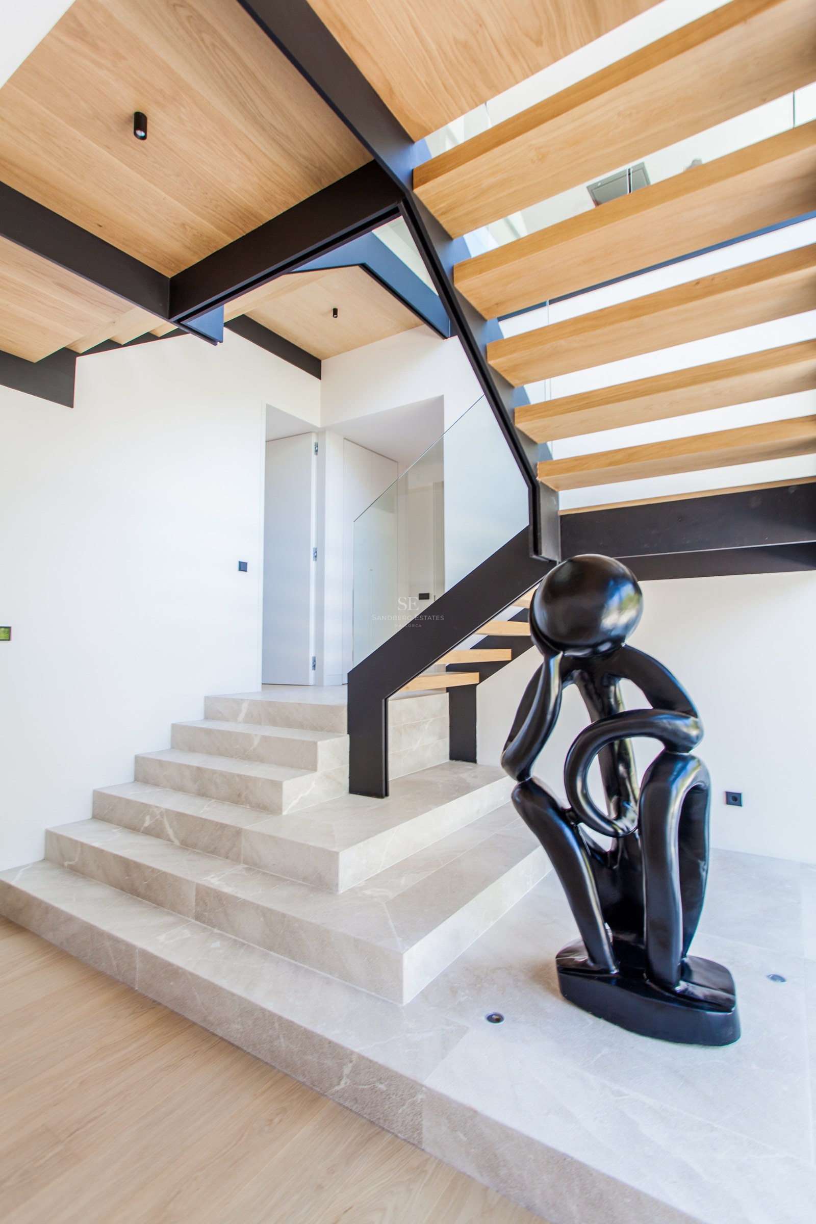 Moderne Treppe mit Steinstufen, schwarzem Stahlrahmen und Holzelementen neben einer schwarzen abstrakten Skulptur.