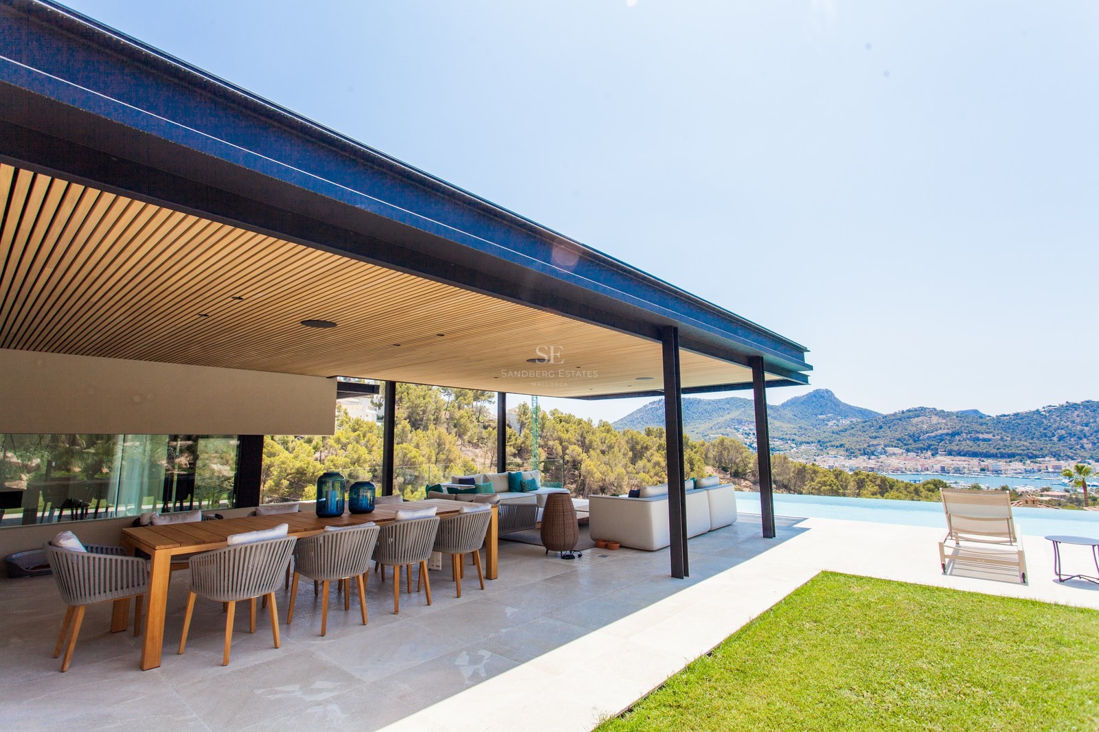 Luxuriöse Außenterrasse mit großem Holzesstisch, Lounge-Bereich und Infinity-Pool mit Blick auf die Bucht.