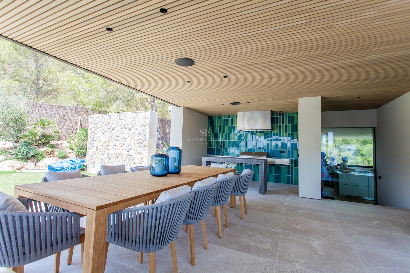 Moderne Terrasse mit großem Holztisch, Seilstühlen und einer voll ausgestatteten Außenküche mit grünen Fliesen.