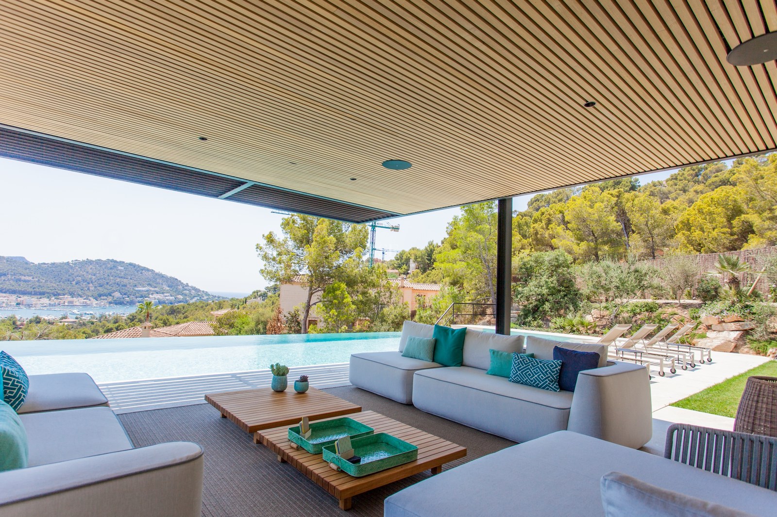 Moderne Terrasse mit grauen Sofas, Holzlattenendecke und Infinity-Pool mit Blick auf Küste und Berge.