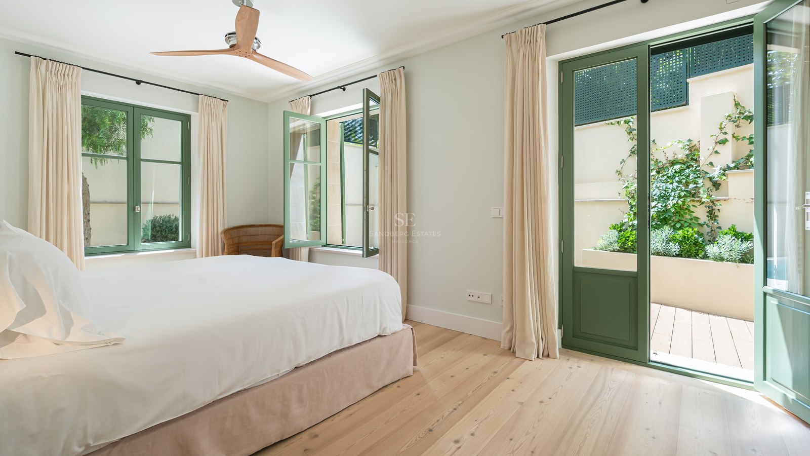 Dormitorio luminoso con suelos de madera clara, carpintería verde y acceso directo a un patio privado.
