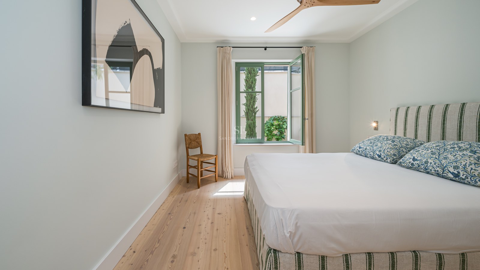 Dormitorio luminoso con suelos de madera clara, marcos de ventana verde salvia y textiles de lino natural.