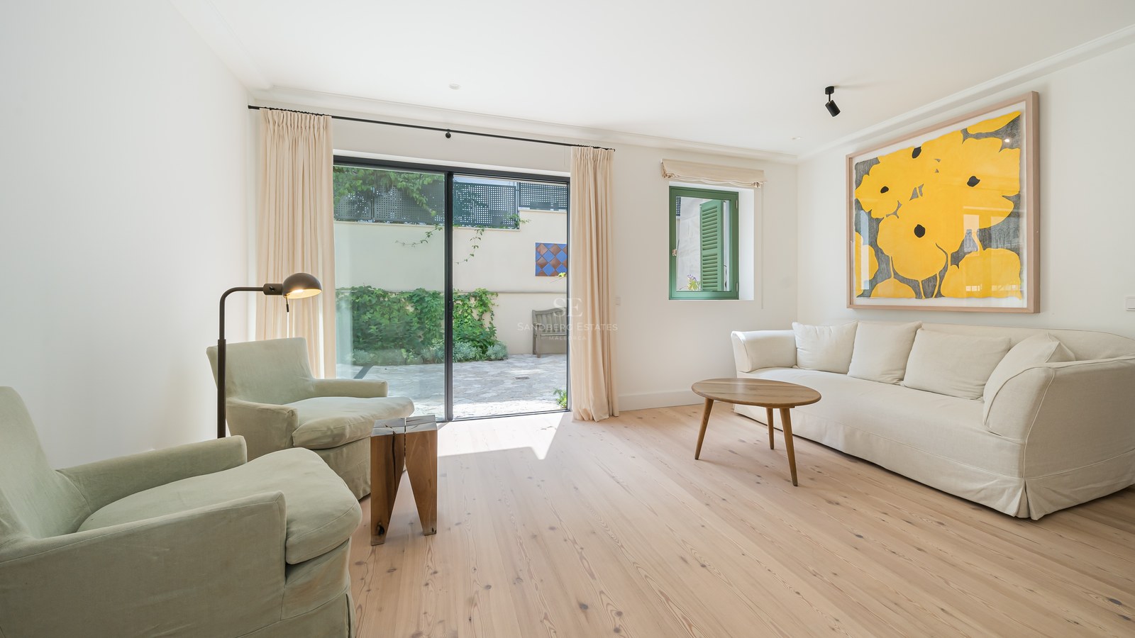 Salón moderno con suelos de roble claro, muebles en tonos crema y grandes puertas correderas de cristal hacia un patio.