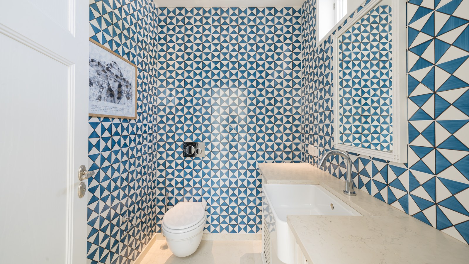Baño pequeño con azulejos geométricos azules y blancos, sanitario suspendido y lavabo minimalista.