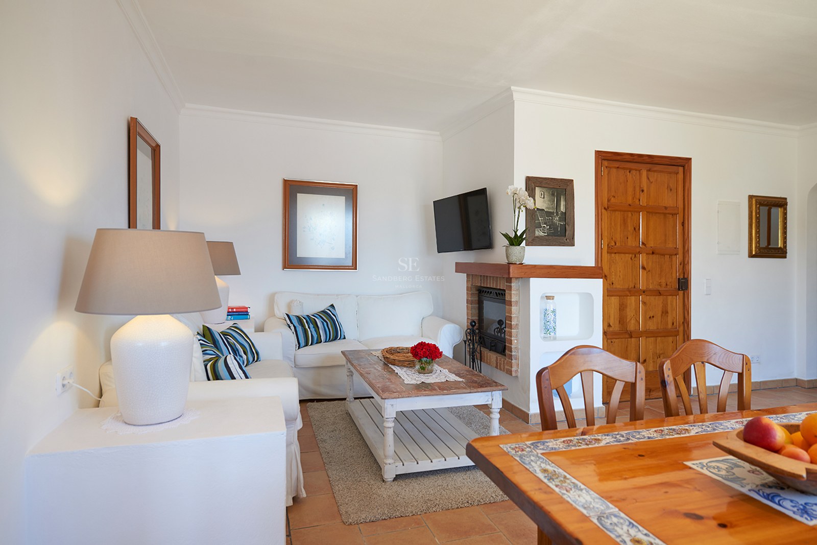 Helles Wohnzimmer mit weißen Sofas, rustikalem Couchtisch aus Holz, Kamin und Terrakottaboden.