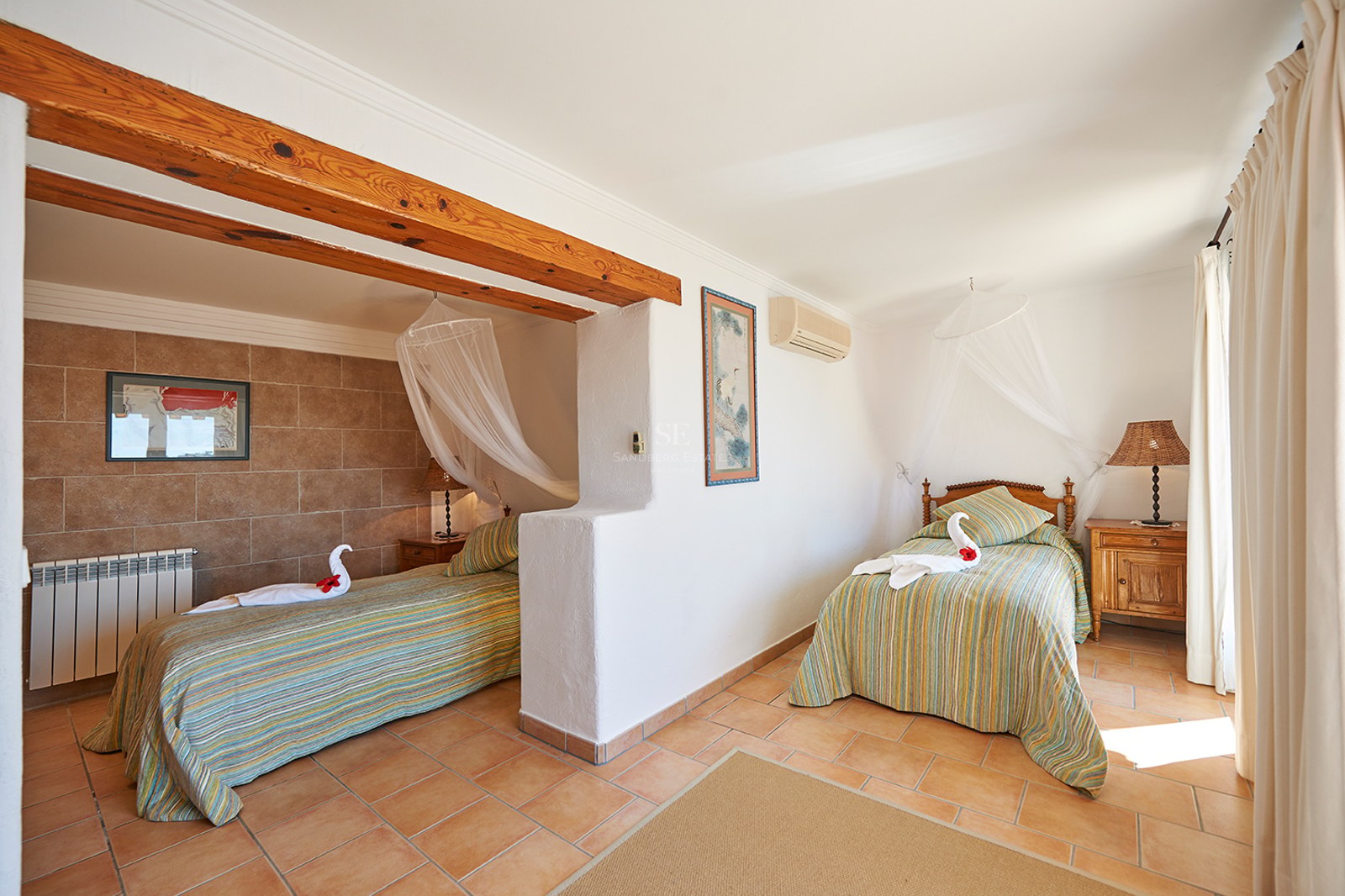 Helles Schlafzimmer mit zwei Einzelbetten, Moskitonetz-Baldachinen, Holzbalken und Terrakottaboden.