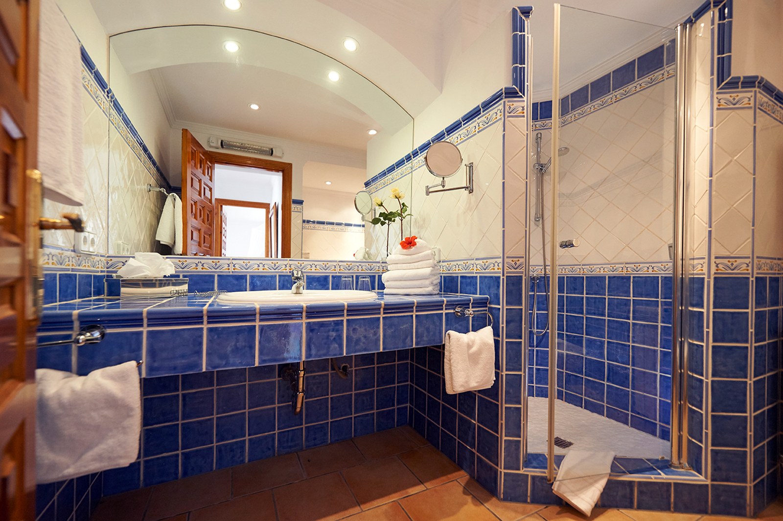 Blau-weiß gefliestes Badezimmer mit einem großen Rundbogenspiegel und einer gläsernen ebenerdigen Dusche.