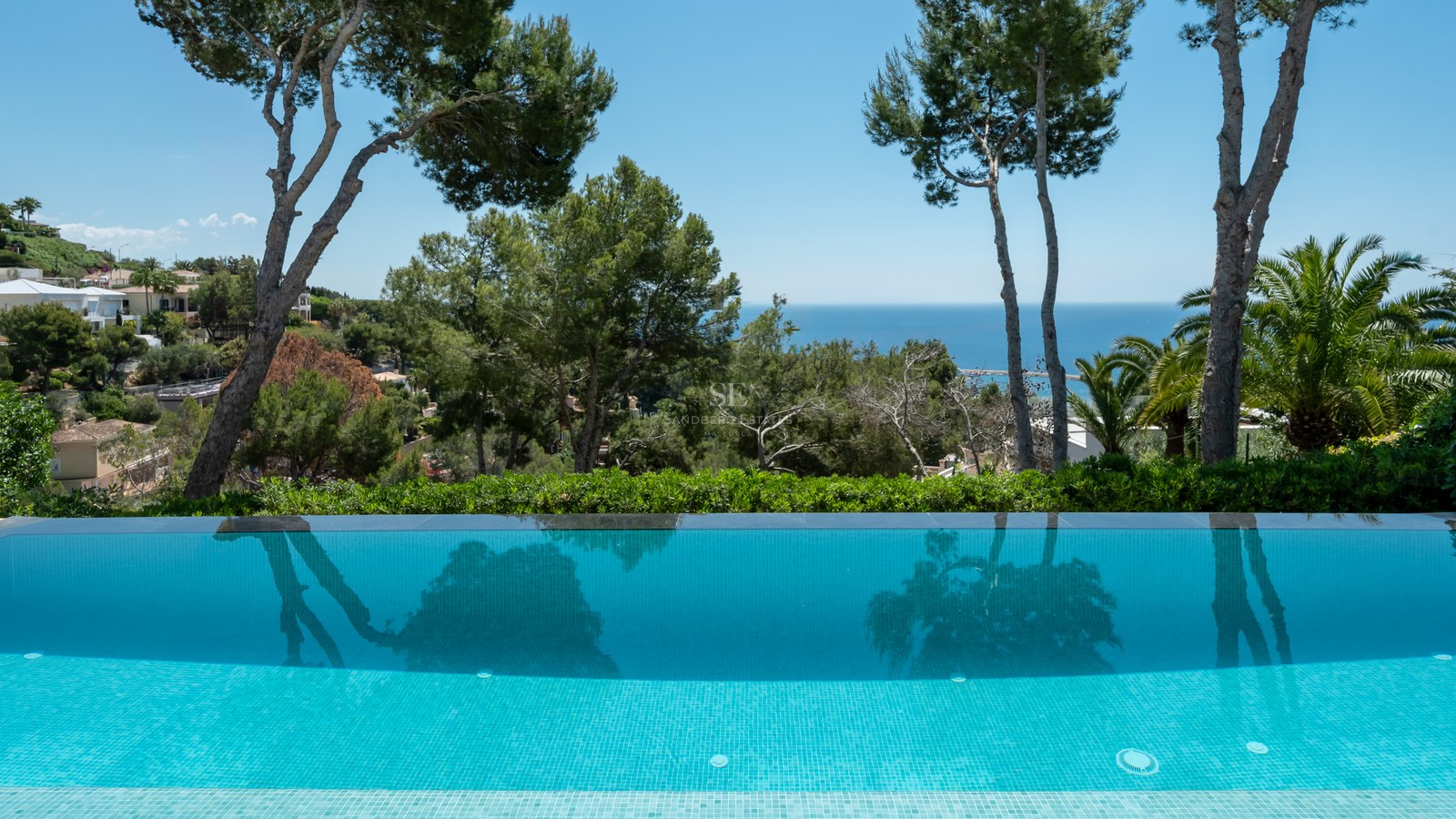 Infinity-pool som speglar tallar, med utsikt över ett grönt landskap och det blå Medelhavet.