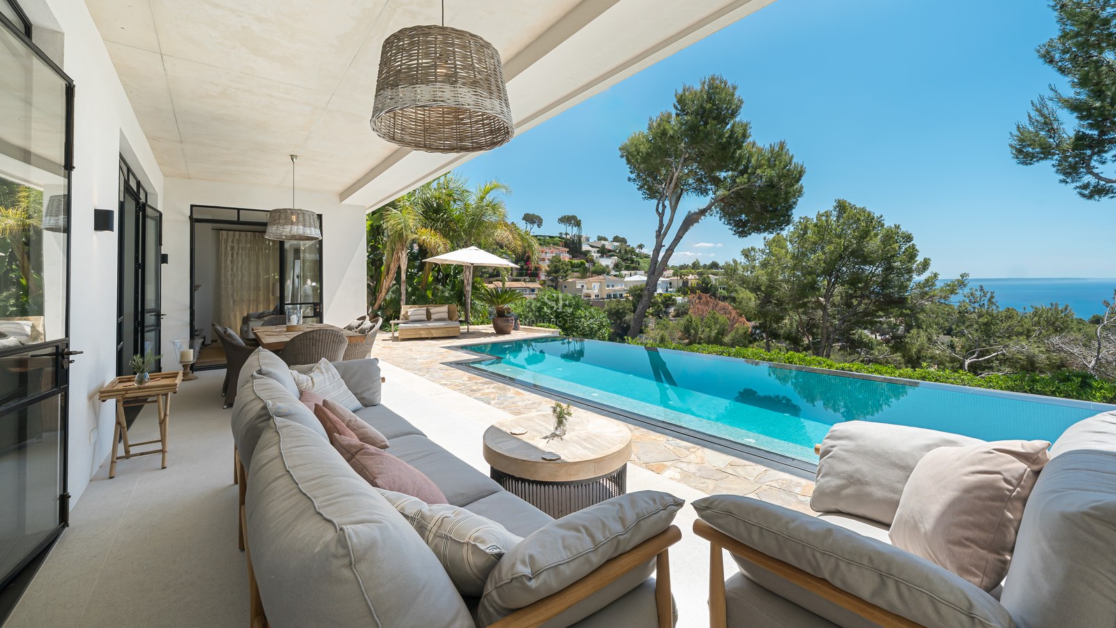 Övertäckt terrass med grå loungemöbler som vetter mot en turkos infinitypool och Medelhavet.
