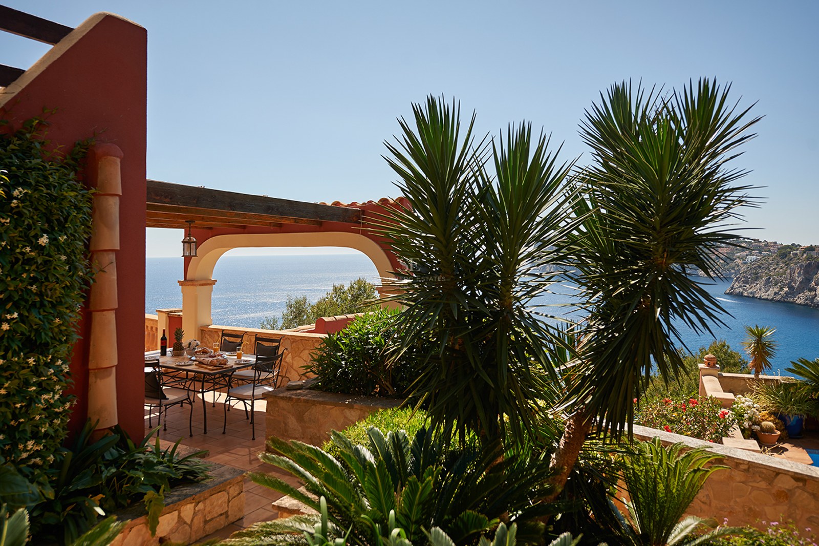 Matplats utomhus på en terrass i terrakotta med bågformad pergola och panoramautsikt över havet.