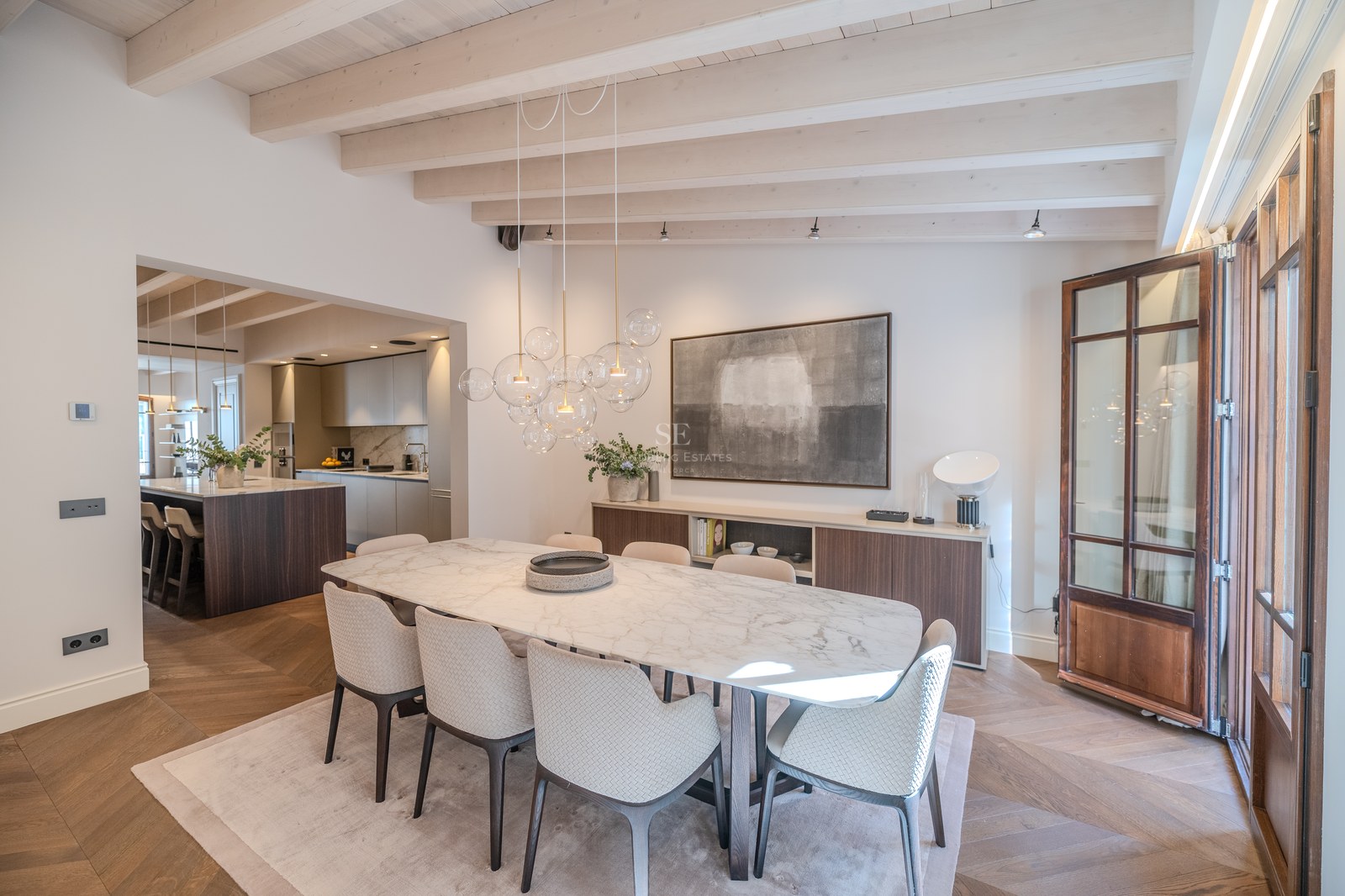 Salle à manger moderne avec table en marbre, lustre designer en verre et poutres apparentes blanchies.