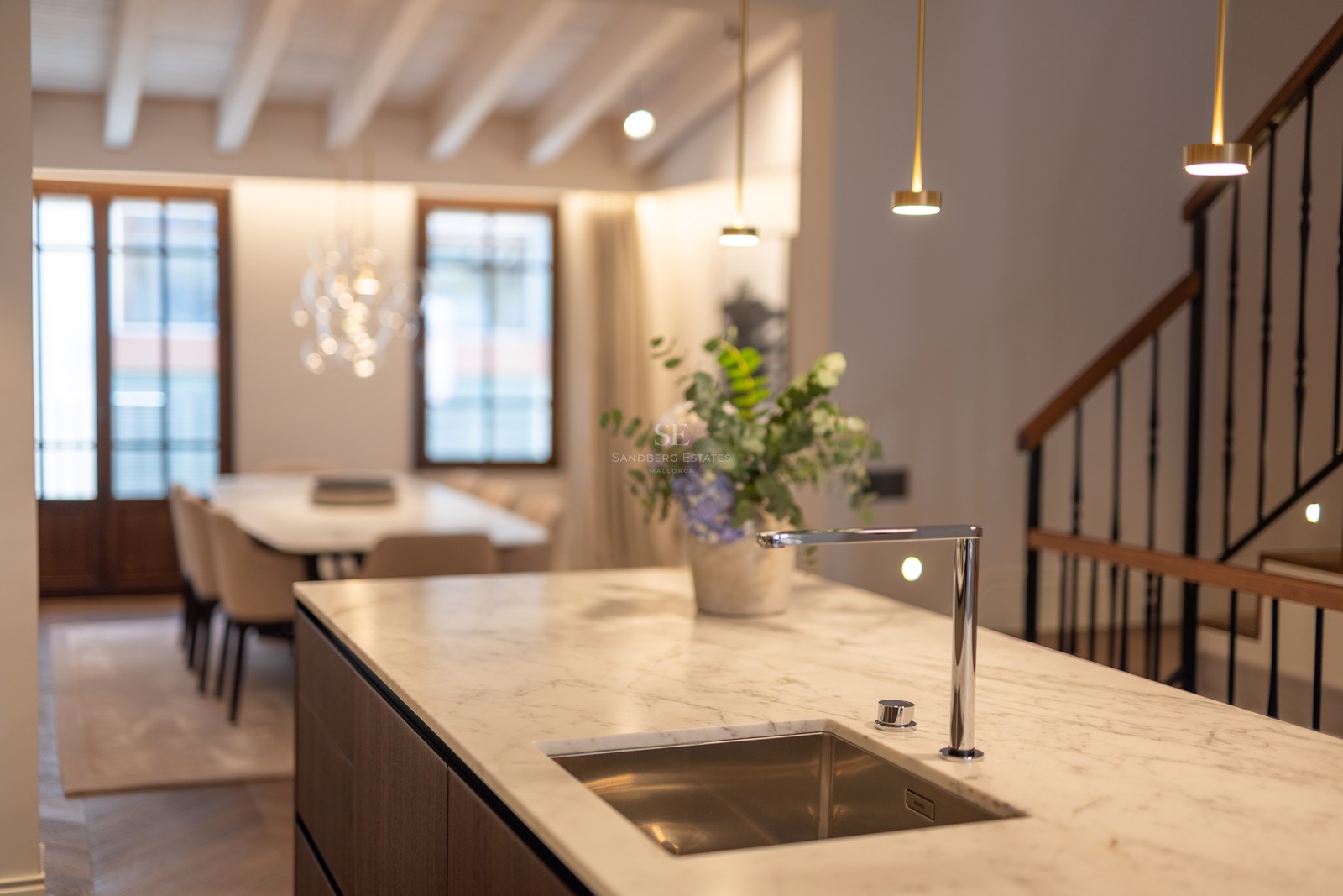 Îlot de cuisine moderne avec comptoir en marbre blanc, robinet chromé et évier intégré, face à la salle à manger.